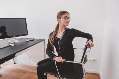 Business Yoga, Frau auf einem Bürostuhl mit einer seitlichen Rotation im Brustkorb, um die Wirbelsäule zu mobilisieren und den Brustkorb zu dehnen.